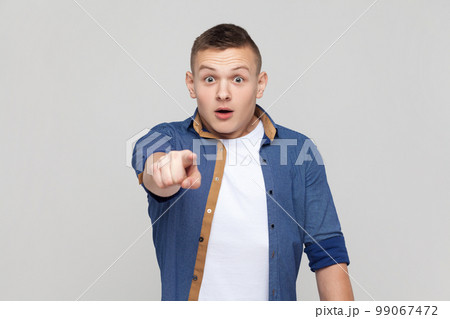 Portrait of astonished amazed handsome teenager boy wearing blue shirt pointing to camera with surprised shocked expression, making choice. Indoor studio shot isolated on gray background. 99067472