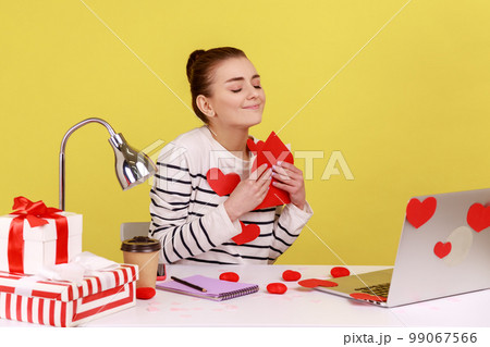 Portrait of romantic woman office manager being touched with sensitive letter, reading Valentine's Day congratulations, sitting on workplace. Indoor studio studio shot isolated on yellow background. 99067566