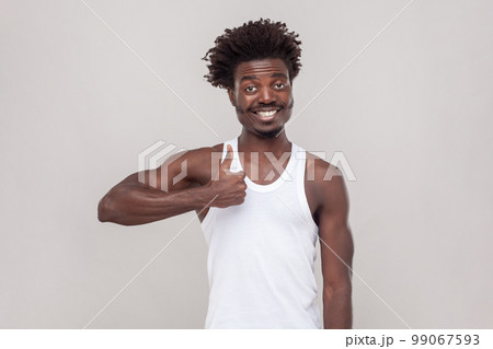 Nice joke. Man with Afro hairstyle showing like gesture, satisfied with something, being in good mood, shows her agreement, wearing white T-shirt. Indoor studio shot isolated on gray background. 99067593