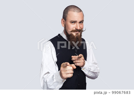 Portrait of joyful cheerful attractive man with beard and mustache indicating both index fingers at camera, saying he needs you, choosing. Indoor studio shot isolated on gray background. 99067683