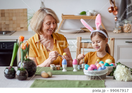 Happy easter family elderly grandmother and little granddaughter with rabbit ears are preparing for the holiday to paint eggs 99067917