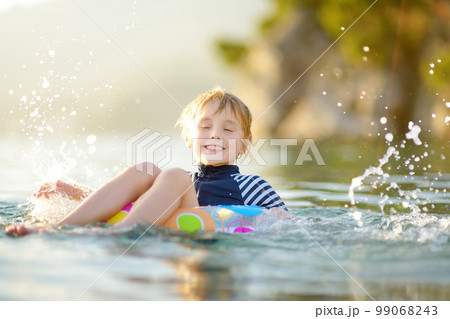 Little boy swimming with colorful floating ring in sea on sunny summer day. Cute child playing in clean water. Family and kids resort holiday during summer vacations. 99068243