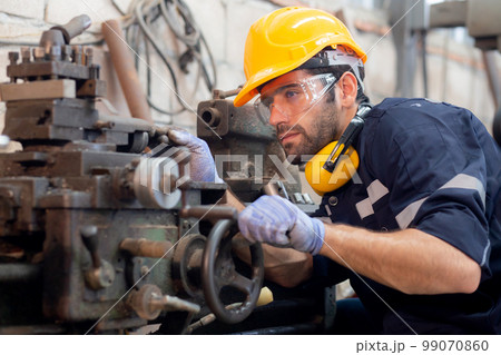Young caucasian engineer man operating lathe machine for preparing production at factory industrial. 99070860