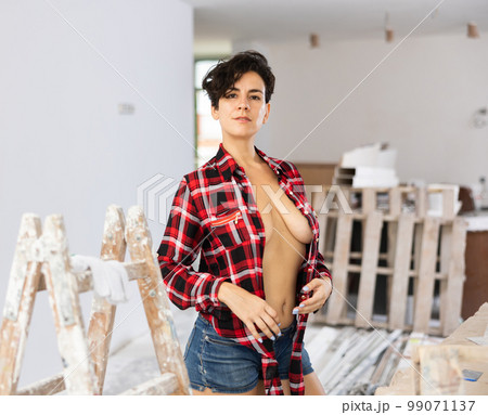 Young brunette in checkered shirt and shorts standing in house being renovated 99071137