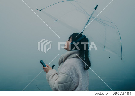 街バックに傘をさして音楽を聴く女性の写真 街バックに傘をさして音楽を聴く女性の写真 99073484