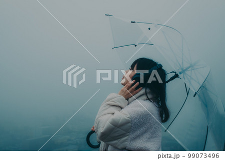 街バックに傘をさして音楽を聴く女性の写真 99073496