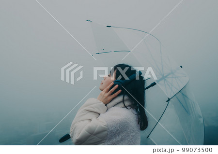 街バックに傘をさして音楽を聴く女性の写真 99073500
