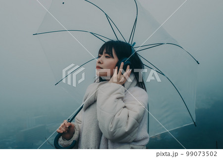 街バックに傘をさして音楽を聴く女性の写真 街バックに傘をさして音楽を聴く女性の写真 99073502