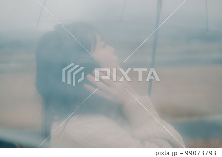 河川敷で傘をさしてスマホをさわる女性の写真 99073793