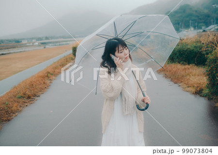河川敷で傘をさしてスマホをさわる女性の写真 河川敷で傘をさしてスマホをさわる女性の写真 99073804