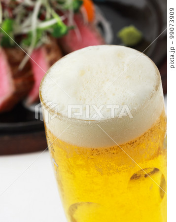 泡立つジョッキのビールとおつまみ 99073909