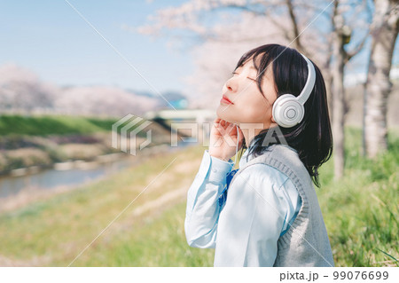 桜の木の下で音楽を聴く高校生 99076699