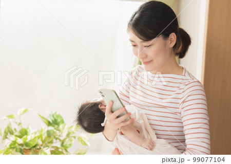 赤ちゃんを抱っこしながらスマホ見るママ 99077104