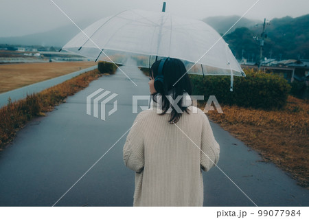 河川敷で傘をさして音楽を聴く女性の写真 河川敷で傘をさして音楽を聴く女性の写真 99077984