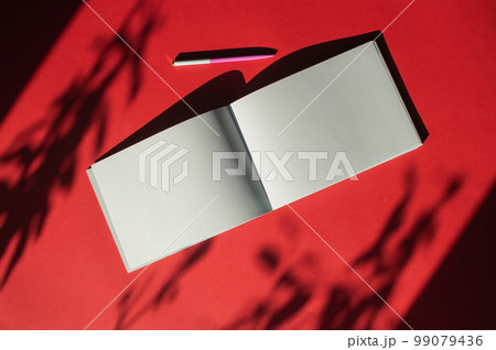 A notepad with a pen lies on a colored red background. Office supplies. Place for text 99079436