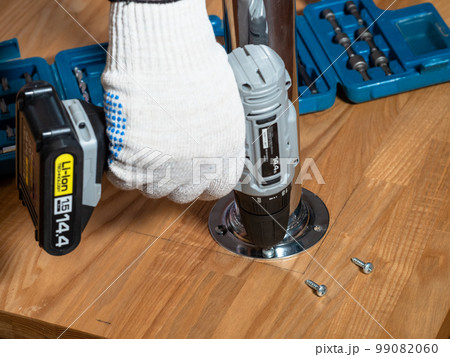 worker screwing screws into wooden board of table worker screwing screws into wooden board of table 99082060