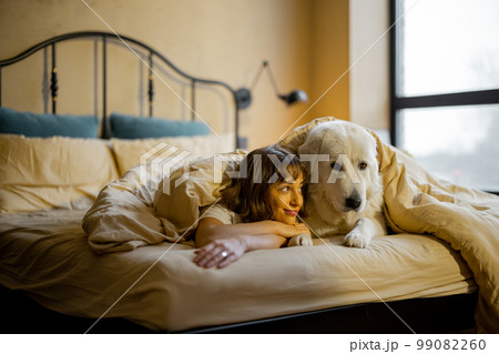 Woman with her dog under the blanket on bed Woman with her dog under the blanket on bed 99082260
