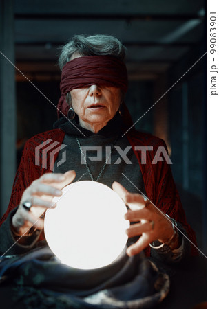 Blindfolded witch fortune teller doing predictions with illuminated crystal ball Blindfolded witch fortune teller doing predictions with illuminated crystal ball 99083901