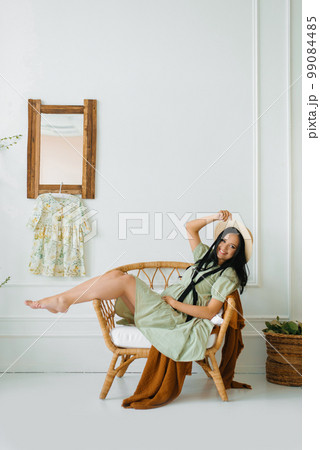 Beautiful pregnant woman smiles while lying on a wicker chair at home 99084485