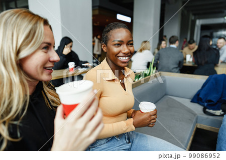 Two young women friends enjoying coffee together in a coffee shop Two young women friends enjoying coffee together in a coffee shop 99086952