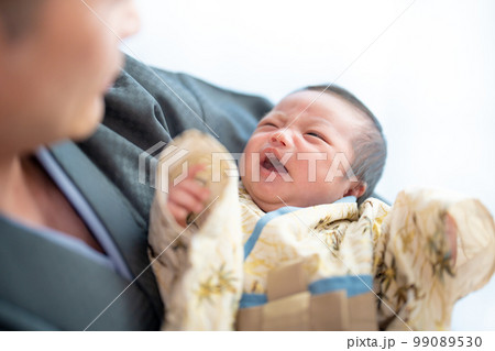 お宮参りの日に着物姿で泣いているところをお父さんに抱かれてあやされる赤ちゃん 99089530