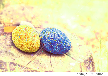 Yellow and blue Easter eggs on a stump in a haze meadow on a sunny bright day Yellow and blue Easter eggs on a stump in a haze meadow on a sunny bright day 99090649