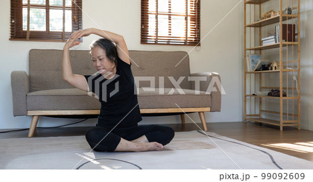 Healthy and elderly woman in workout clothes practicing yoga in her living room 99092609