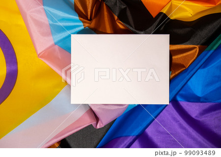 Empty paper blank on Rainbow LGBTQIA flag made from silk material. Mock up template copy space for your text. Symbol of LGBTQ pride month. Equal rights. Peace and freedom. Support LGBTQIA community 99093489