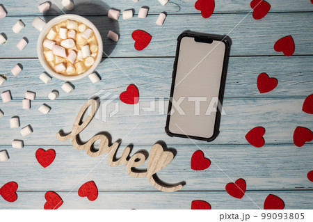 Greeting or invitation white screen on mobile phone mock up with white cup of coffee and marshmallows on wooden background. Romantic Small hearts Valentine day. Blank card copy space for your text. Greeting or invitation white screen on mobile phone mock up with white cup of coffee and marshmallows on wooden background. Romantic Small hearts Valentine day. Blank card copy space for your text. 99093805