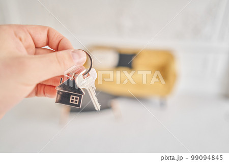 Men hand holding key with house shaped keychain. Modern light lobby interior. Mortgage concept. Real estate, moving home or renting property. 99094845