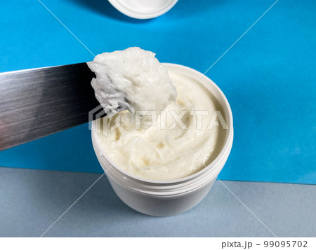 white jar with cream and spatula close up on blue 99095702