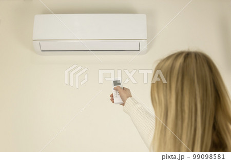 Back view of a woman controlling the air temperature in the house with a remote control. Home air conditioning concept. Back view of a woman controlling the air temperature in the house with a remote control. Home air conditioning concept. 99098581
