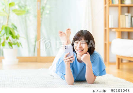 リビングでスマートフォンを使う若い女性 リビングでスマートフォンを使う若い女性 99101048
