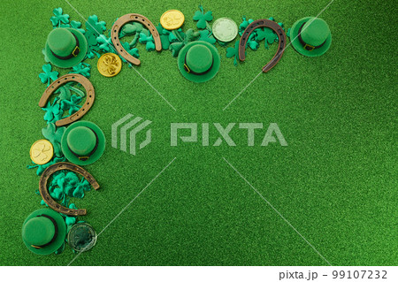 St Patricks Day corner border of shamrocks, gold coins and leprechaun hat over a glittery green background 99107232
