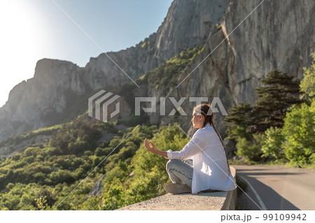 Profile of a woman doing yoga in the top of a cliff in the mountain. Woman meditates in yoga asana Padmasana 99109942