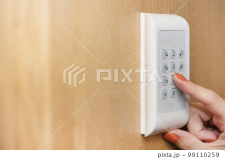 Alarm panel. The hand enters the code from the house security alarm. Real estate security, home security system. Alarm panel. The hand enters the code from the house security alarm. Real estate security, home security system. 99110259