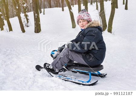 A boy rides a snow scooter outdoors in winter. Winter vacation and holidays A boy rides a snow scooter outdoors in winter. Winter vacation and holidays 99112187
