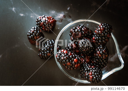 Top view of a Serving of real Blackberries in a small clear bowl on a black granite surface.Horizontal orientation, space for text. Dark food. Top view of a Serving of real Blackberries in a small clear bowl on a black granite surface.Horizontal orientation, space for text. Dark food. 99114670