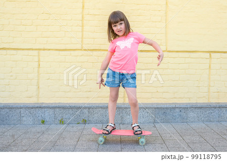 Stylish, little girl with a skateboard on a background of a yellow wall, posing for the camera 99118795