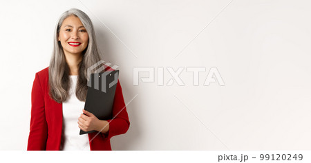 Successful asian senior business woman holding clipboard, wearing red blazer and lipstick at work, smiling at camera, white background Successful asian senior business woman holding clipboard, wearing red blazer and lipstick at work, smiling at camera, white background 99120249