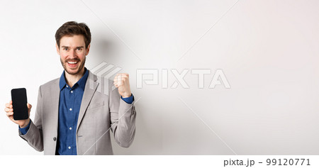 E-commerce and online shopping concept. Man making money in internet, showing smartphone screen and winner gesture, smiling satisfied, standing on white background E-commerce and online shopping concept. Man making money in internet, showing smartphone screen and winner gesture, smiling satisfied, standing on white background 99120771
