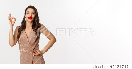 Beautiful young woman with red lipstick, wearing glamour glitter dress showing okay sign, approve and like product, praise good work, standing over white background Beautiful young woman with red lipstick, wearing glamour glitter dress showing okay sign, approve and like product, praise good work, standing over white background 99121717