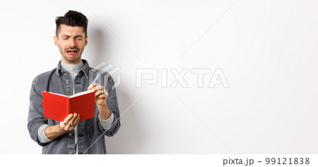 Sad crying guy writing in his diary with miserable face, look distressed while making notes in journal or planner, standing against white background Sad crying guy writing in his diary with miserable face, look distressed while making notes in journal or planner, standing against white background 99121838
