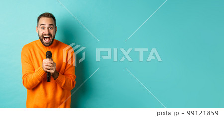 Handsome adult man perform song, singing into microphone, standing against turquoise background 99121859
