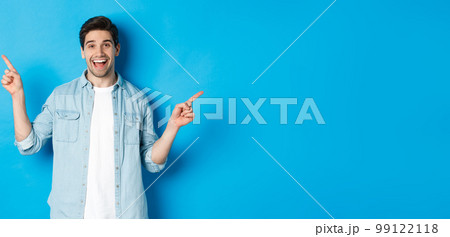 Cheerful adult man smiling, pointing fingers sideways, showing left and right promo banners, standing against blue background Cheerful adult man smiling, pointing fingers sideways, showing left and right promo banners, standing against blue background 99122118