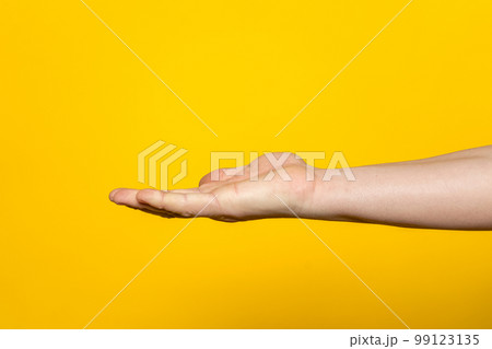 Strong hand of man with palm up presenting an imaginary product in advertising concept isolated on yellow background. 99123135