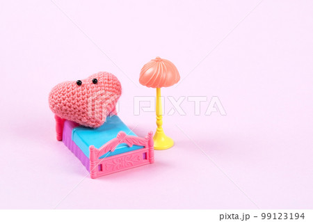 Pink knitted heart with a cute face relaxes on the bed. Love concept. Staged life story of a heart in its room Pink knitted heart with a cute face relaxes on the bed. Love concept. Staged life story of a heart in its room 99123194