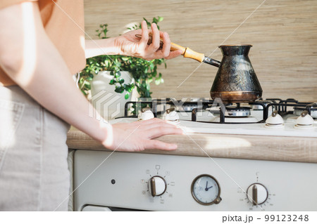 close-up of a woman standing in kitchen preparing Turkish coffee in morning for breakfast. close-up of a woman standing in kitchen preparing Turkish coffee in morning for breakfast. 99123248