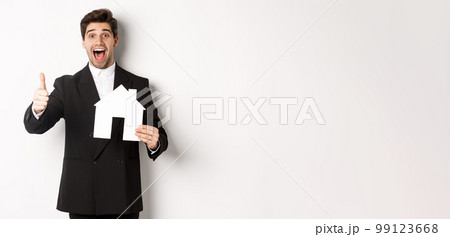 Portrait of excited handsome man looking for a home, showing house and thumb-up, recommending real estate agency, standing against white background Portrait of excited handsome man looking for a home, showing house and thumb-up, recommending real estate agency, standing against white background 99123668