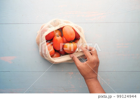 fresh tomato in a reusable shopping bag on table  99124944
